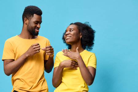 Happy young couple in matching yellow shirts, smiling and interacting playfully against a vibrant blue background, conveying joy and connectionの写真素材
