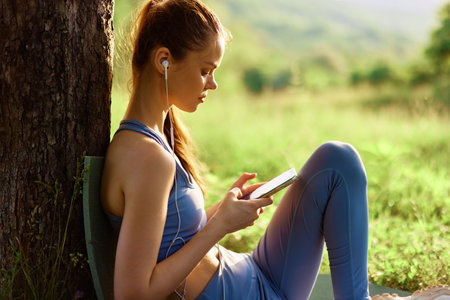 Young woman in athletic clothing enjoying music on a tablet outdoors in nature, conveying relaxation...