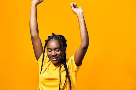 Happy girl with braids celebrating against a bright yellow background, wearing a cheerful yellow t...
