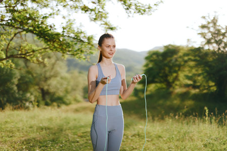 Young woman in sportswear skipping rope outdoors, exuding joy and energy in a sunny, green...