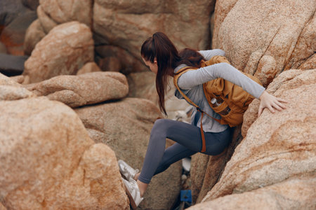 A determined young woman with a backpack navigating rocky terrain, showcasing adventure, perseverance, and exploration in a natural settingの写真素材