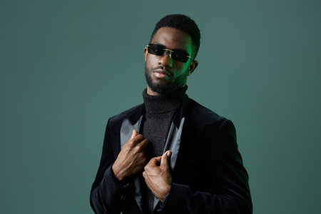 Stylish man in sunglasses and black attire poses confidently against vibrant green background