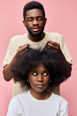 A man styling a woman s natural hair with care against a soft pink background, showcasing the beauty of Afro textured hair and emotional connectionの写真素材