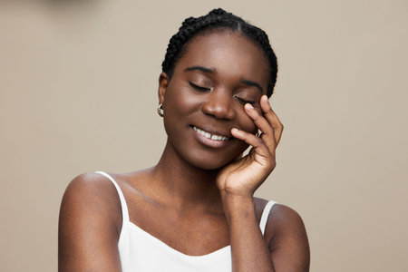 Young African woman with closed eyes smiling gently, wearing a simple white dress, exuding happiness...