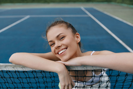 Smiling young woman enjoying tennis on a vibrant blue court, showcasing health and happiness, perfect for sports themed contentの写真素材