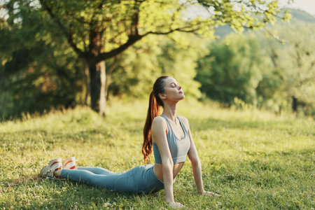 Young fit woman practicing yoga in a serene green park, showcasing flexibility and serenity while...