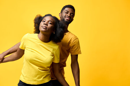 Young African American couple joyfully posing together on a yellow background, showcasing vibrant clothing and playful emotionsの写真素材
