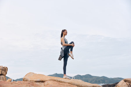 Fit young woman practicing yoga on rocky terrain in athletic wear, showcasing strength and balance...