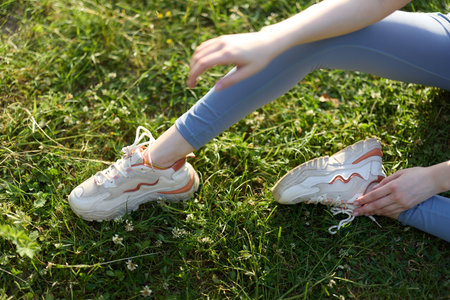 A young woman in stylish athletic shoes sitting on green grass, showcasing relaxation and outdoor...