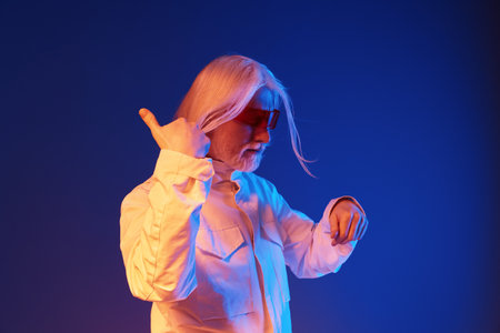 Confident older man with long silver hair in sunglasses posing in vibrant lighting His playful...