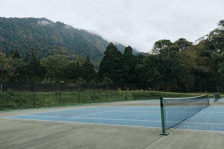 Empty tennis court surrounded by lush greenery and misty mountains, perfect for serene sports photography in a tranquil environmentの写真素材