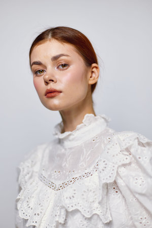 Elegant young woman with a thoughtful expression, wearing a white ruffled blouse, against a soft, neutral background, conveying a sense of beauty and serenityの写真素材