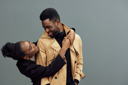 Young African couple sharing a joyful moment, dressed in trendy clothing, set against a neutral gray...