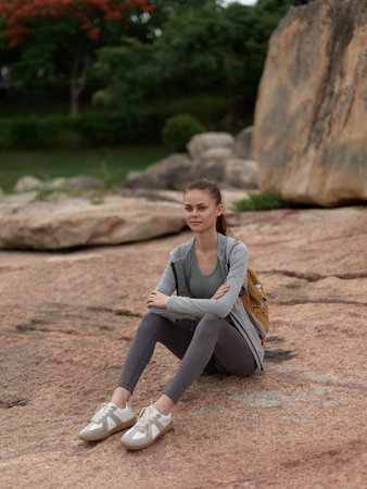 Young woman in activewear sitting on rocky terrain, displaying a pensive expression, perfect for fitness and outdoor themesの写真素材