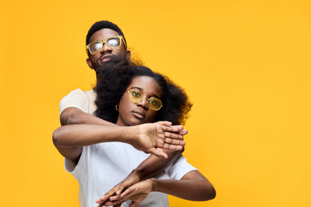 Stylish young couple with sunglasses posing against a vibrant yellow background, showcasing love and confidence with a playful vibe, perfect for fashion and lifestyle conceptsの写真素材