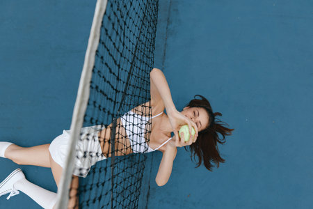 Happy young woman playing tennis on a blue court, wearing a sporty outfit and enjoying her game with a bright smile, perfect for sports and fitness themesの写真素材