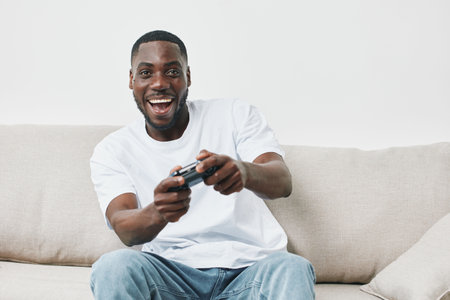 Happy young African American man playing video games at home, showcasing excitement and joy in a...