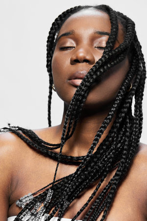 Beautiful woman with braided hair, closed eyes, serene expression, wearing stylish clothing, minimalist background, showcasing elegance and confidence in beauty fashionの写真素材