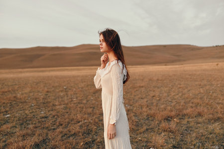 Woman in white dress standing in open field under the bright sunlight, embracing the beauty of natureの写真素材
