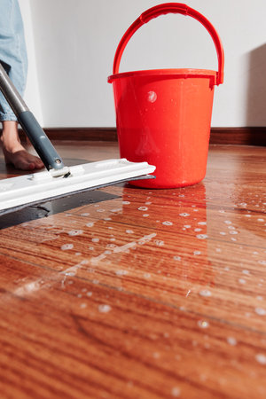 Woman mopping hardwood floor with buckets of water nearbyの写真素材