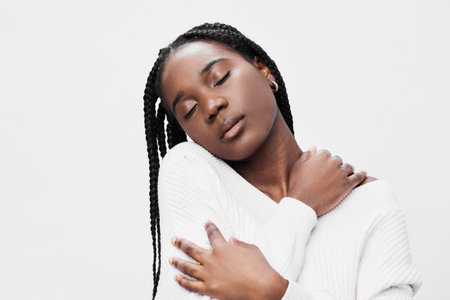 Portrait of a serene young Black woman in a cozy white sweater, expressing tranquility and self love against a minimalist background, ideal for wellness themesの写真素材