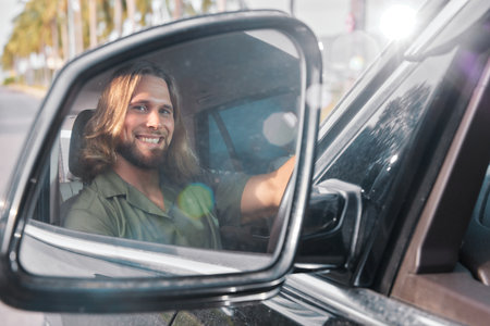 Smiling man in car side mirror, showing joy while driving on a sunny day with palm trees in the backgroundの写真素材