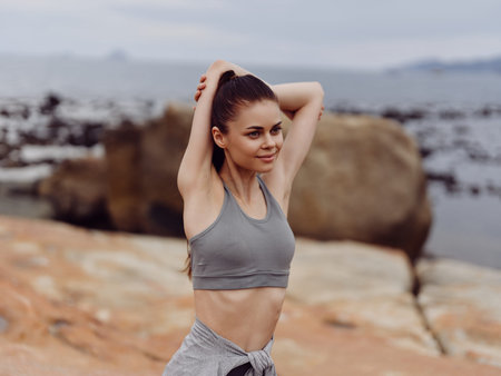 Young woman practicing yoga on the beach in activewear, expressing joy and confidence, with a serene...