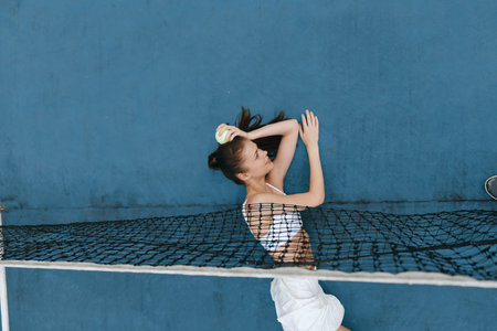 Young woman with long hair brushing her hair while lying on a net against a blue wall, showcasing...