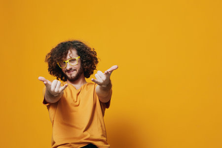 Cheerful young man with curly hair in yellow glasses on a vibrant orange background, expressing joy and positivity while wearing a casual shirtの写真素材