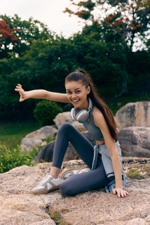 Active young woman enjoying outdoor workout in sporty attire, smiling and stretching on rocky terrain during a sunny day, showcasing a vibrant lifestyleの写真素材