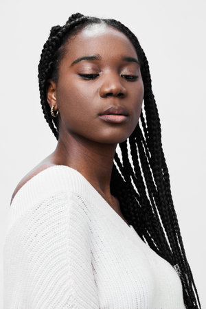 Portrait of a confident Black woman with braids, wearing a white sweater, exuding elegance and serenity against a simple white background, ideal for beauty and fashion conceptsの写真素材