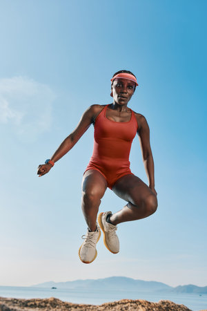 Athletic woman jumping against a clear blue sky wearing a red swimsuit and sports shoesの写真素材