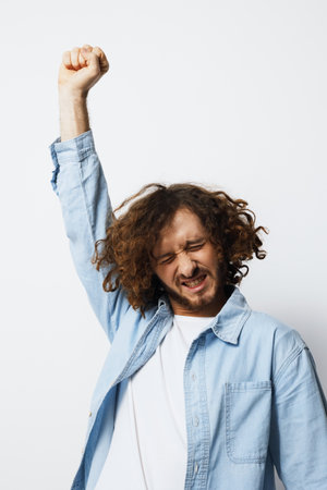 Young man with curly hair celebrating joyfully, wearing a light blue shirt against a white background, expressing excitement and positivity, suitable for motivational themesの写真素材