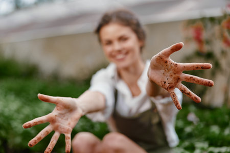 A joyful woman in a garden with dirt covered hands, showcasing her love for gardening and nature, wearing casual clothing and smiling brightly amidst green foliageの写真素材