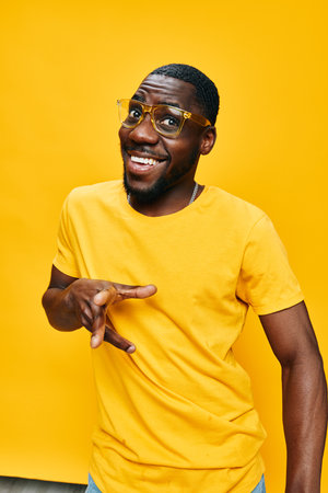 Happy young man smiling in a yellow t shirt and glasses, posing with a playful gesture against a bright yellow background Vibrant colors enhance the cheerful mood of the imageの写真素材