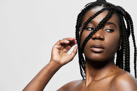 A confident young Black woman with braided hair posing against a minimalist white background, conveying strength and beauty through her expressionの写真素材