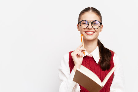 Smiling student with glasses holding a pencil and notebook, dressed in a red sweater, against a plain white background, exuding confidence and curiosity for learningの写真素材