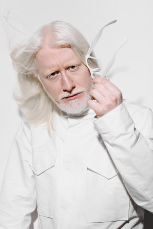 Portrait of an elderly man with long white hair holding glasses, wearing a white outfit against a clean, bright background, exuding a sense of wisdom and confidenceの写真素材