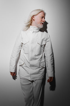 Fashion model in white outfit standing confidently against a minimalistic grey background, exuding modern elegance and style, with a soft light emphasizing the silhouetteの写真素材