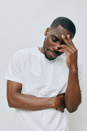 Portrait of a young Black man expressing contemplation, dressed in a casual white shirt, with a neutral background, conveying emotions of introspection and thoughtfulnessの写真素材