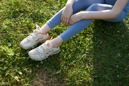 Young woman in activewear sitting on grass, wearing stylish sneakers, expressing relaxation, embodying a healthy lifestyle, vibrant spring colorsの写真素材