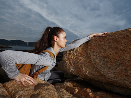 Young woman climbing rocks during outdoor adventure, expressing determination and strength in a natural coastal settingの写真素材
