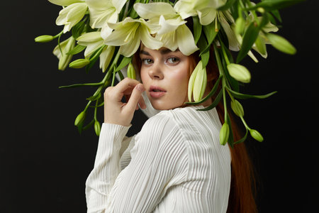 Young woman with long red hair, adorned with a floral crown of white lilies, expressing serenity against a dark background, perfect for concepts of beauty and natureの写真素材