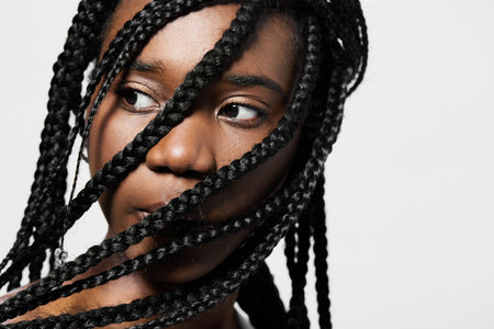 Close up portrait of a young Black woman with braided hair, showcasing her thoughtful expression against a clean white backgroundの写真素材