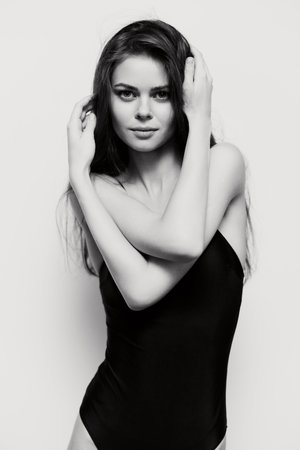 Confident young woman in a black swimsuit posing gracefully against a white background, showcasing...