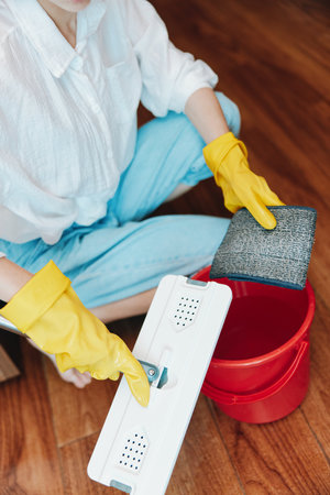 Woman in yellow gloves mopping hardwood floor with bucket of waterの写真素材