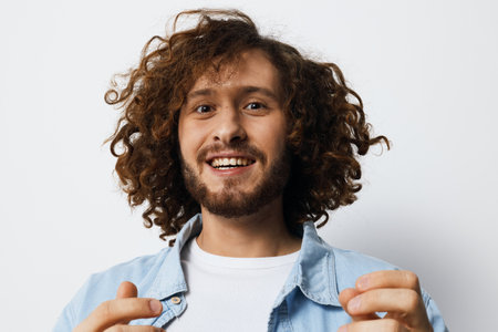 Smiling man with curly hair in denim jacket expressing joy and positivity against a light background, ideal for promoting happiness and connectionの写真素材