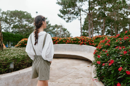 Young woman in casual outdoor outfit enjoying a serene moment in a flower garden, wearing suspenders...