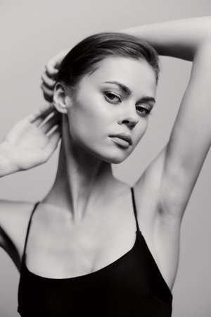 Elegant young woman posing confidently in a classic black outfit, showcasing her graceful neck and facial features against a soft monochrome background.の写真素材