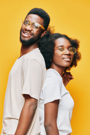 Two smiling models with glasses in casual outfits against a vibrant yellow background, showcasing a...